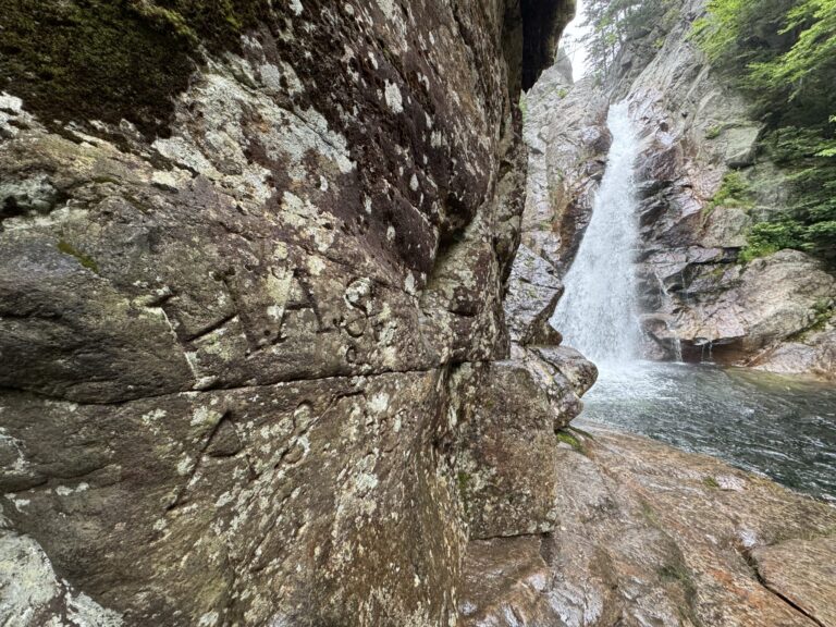 A rock wall at the base of Glen Ellis Falls, New Hampshire, carved with ‘H.A. Seavey and A.P. Thompson, 1876,’ with the waterfall flowing into the riv