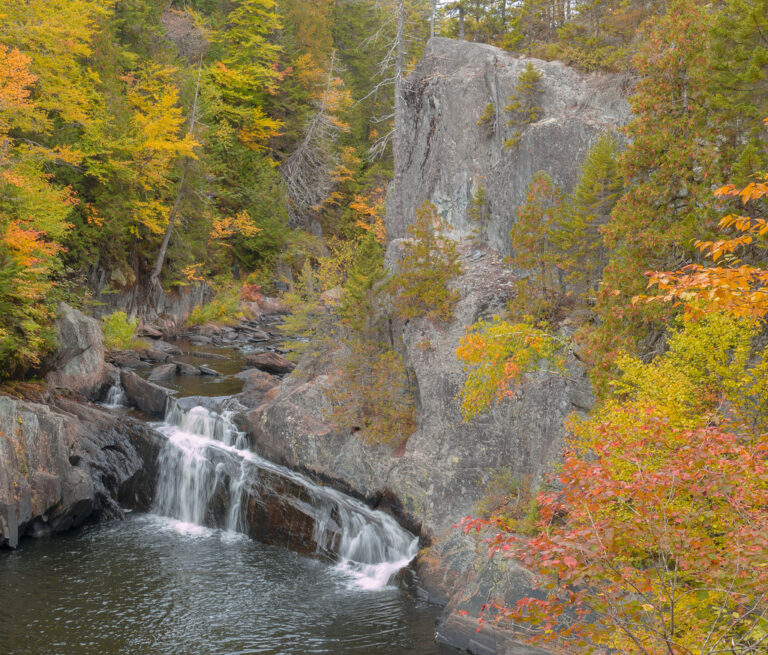 Rich fall foliage cheering up the cliffs of Buttermilk Falls on an overcast October day at Gulf Hagas in Maine.